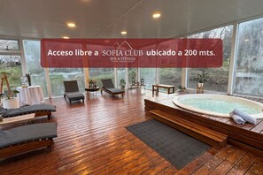 A spacious indoor area with a hot tub, lounge chairs, and a large window offering a view of the outdoors. - Villa Sofia Apart Hotel & Spa (San Carlos de Bariloche)
