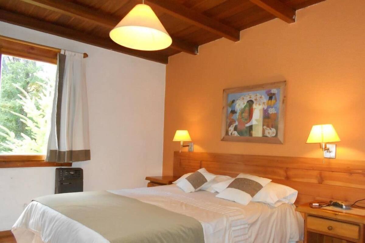Ein Schlafzimmer mit einem Bett, zwei Nachttischlampen, einem Bild an der Wand und einem Fenster mit Vorhängen.