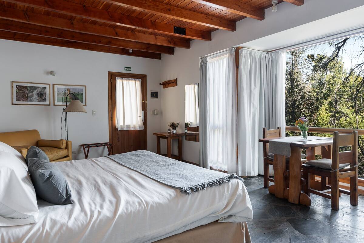 Ein Schlafzimmer mit Bett, Schreibtisch und Stuhl. Eine Tür trägt die Aufschrift 'SALIDA' und ein Fenster mit Vorhängen.