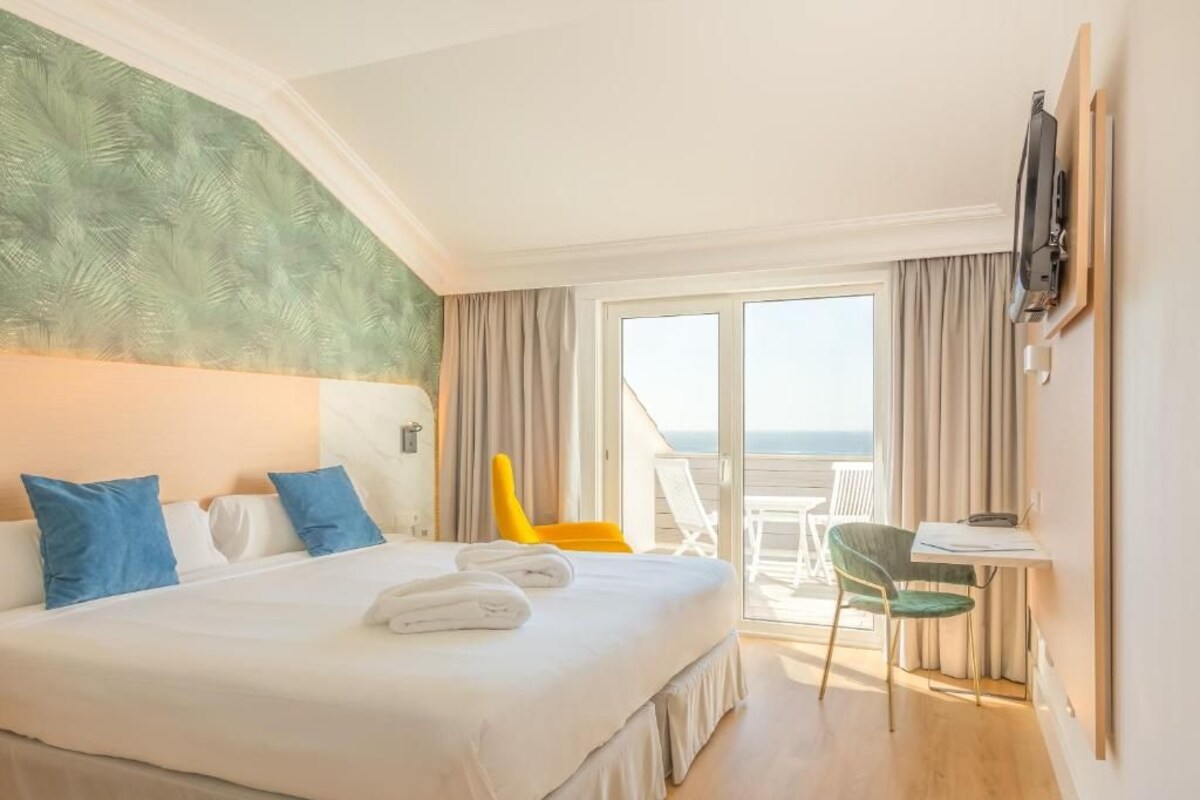 A hotel room with a bed, a desk, a chair, and a view of the ocean.