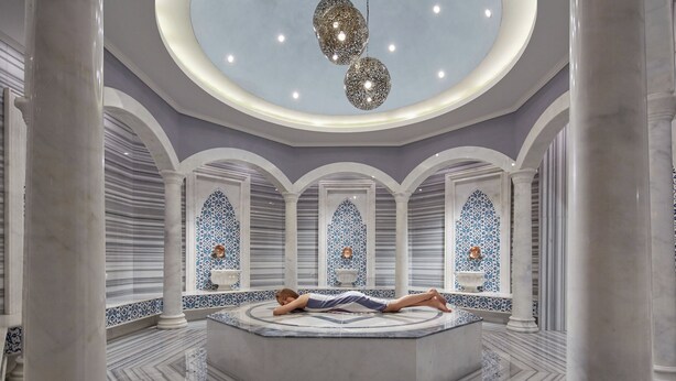Ein luxuriöser Spa-Bereich mit einer zentralen, runden Sitzgruppe, Marmorböden und dekorativen Bögen mit blau-weißen Fliesenmustern.