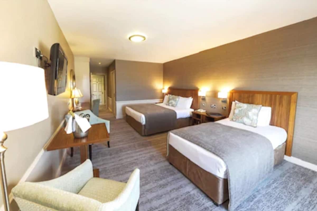 A hotel room with two beds, a desk, a chair, and a nightstand with lamps.