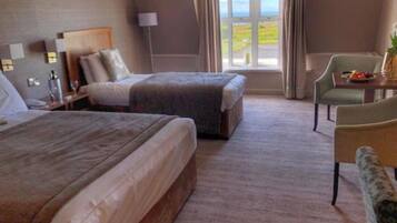 A hotel room with two beds, a sitting area with a chair and table, a lamp, and a window with a view.