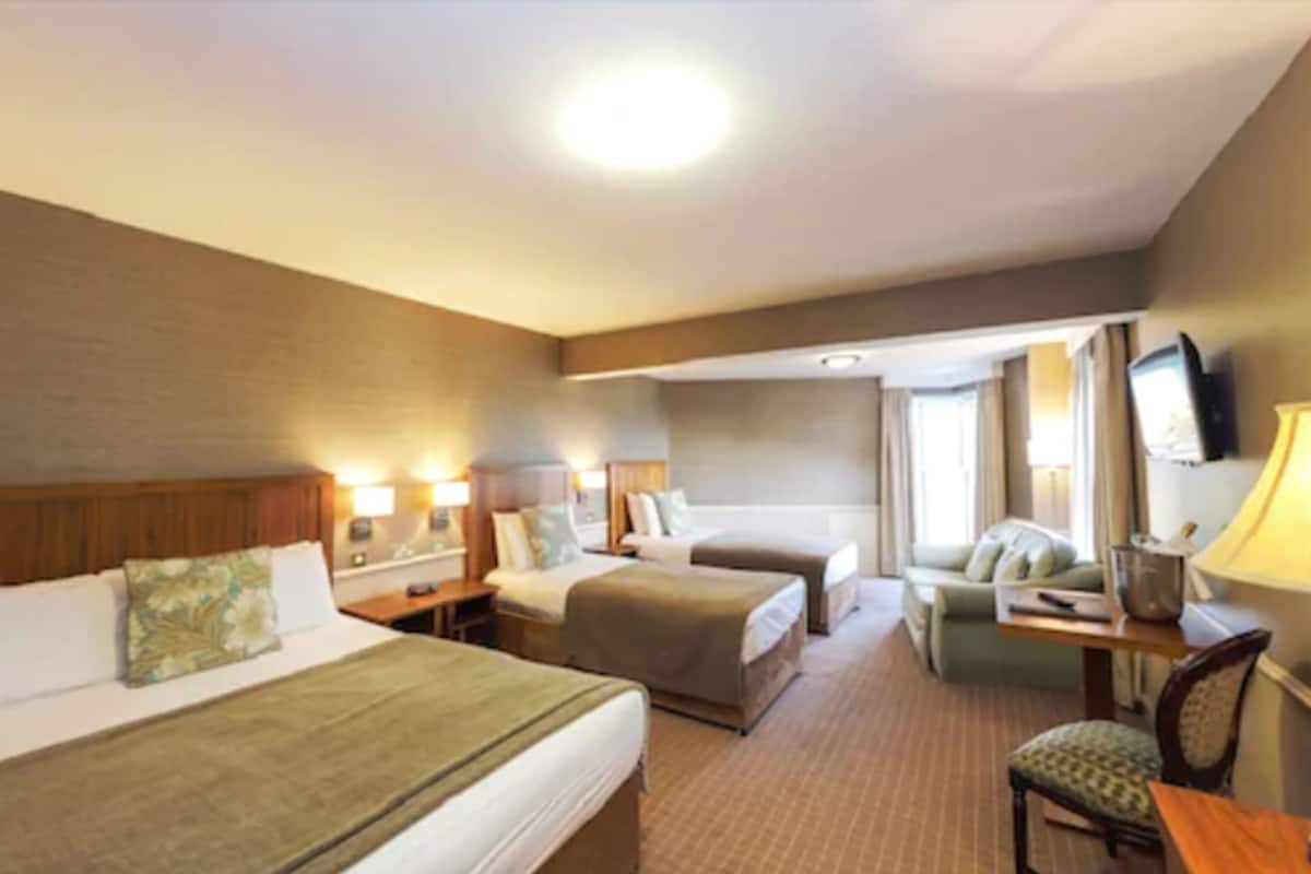 A hotel room with two beds, a sofa, a desk with a lamp, and a television.