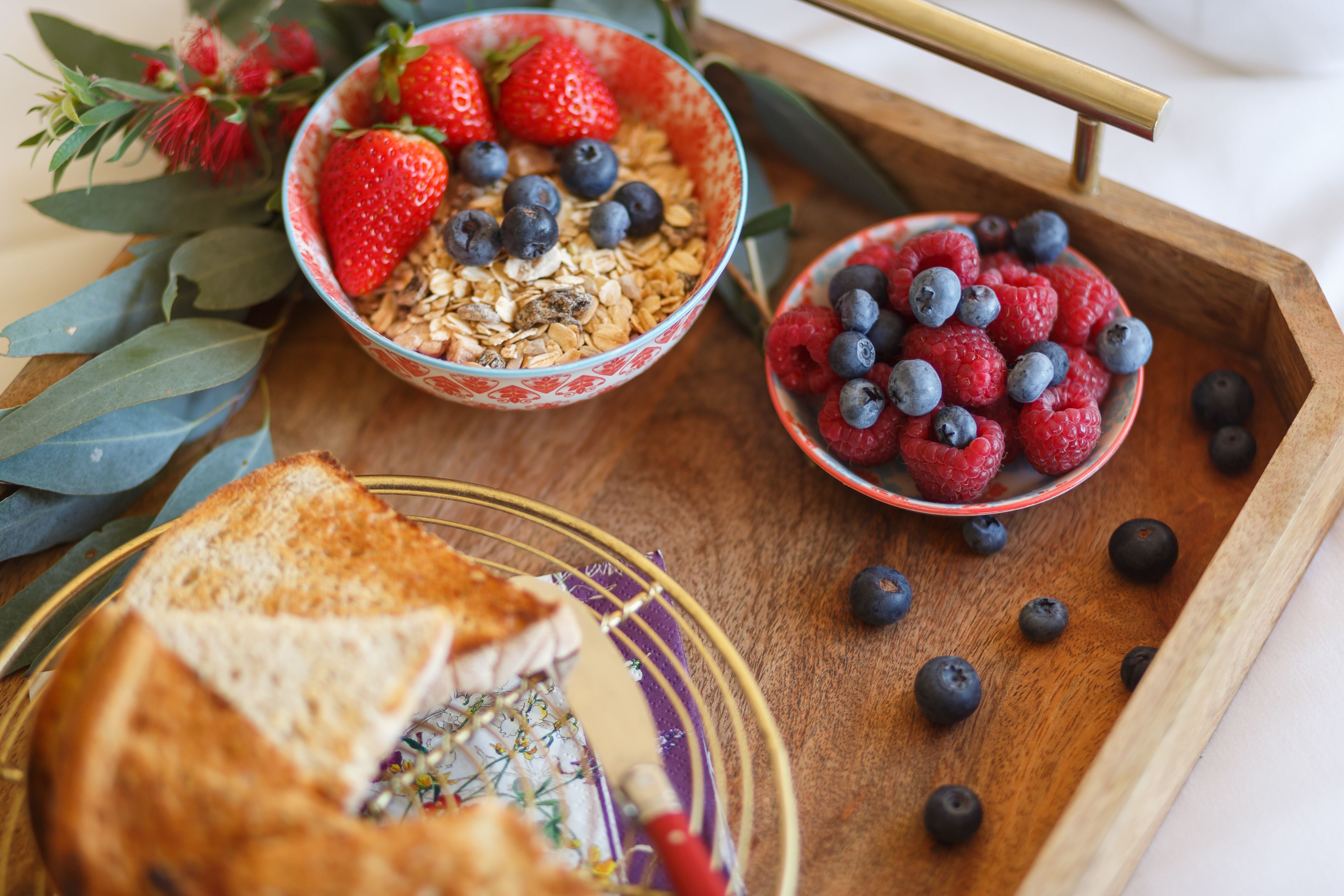 A breakfast tray with cereal, strawberries, blueberries, raspberries, and toast.