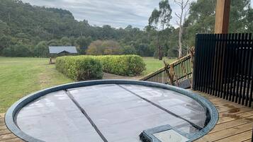 Una vasca idromassaggio su un pontile di legno con vista su un prato e alberi sullo sfondo.