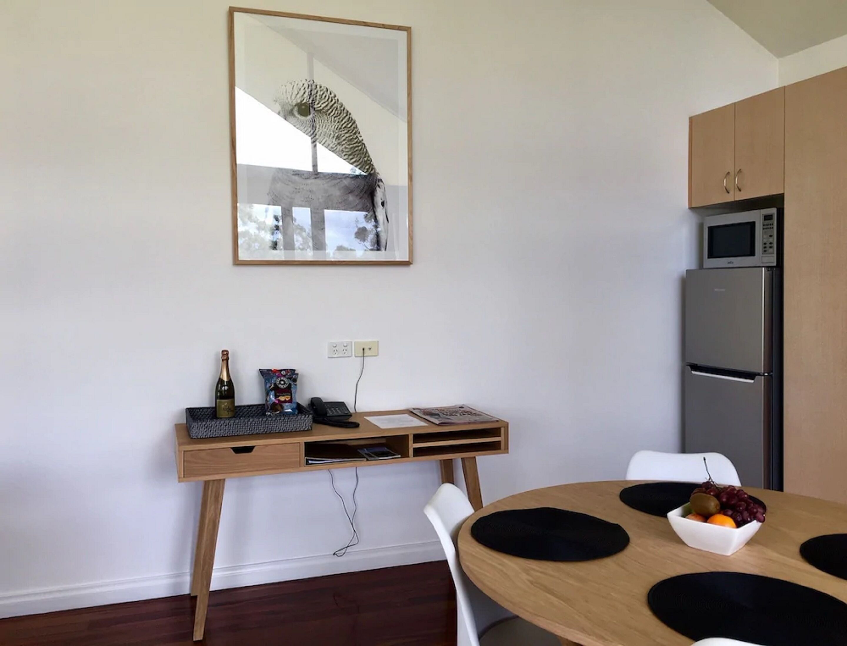 Una cocina moderna con microondas y refrigerador integrados, una mesa de comedor de madera con individuales negros y un escritorio con computadora y una botella de vino.