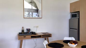 Una cocina moderna con microondas y refrigerador integrados, una mesa de comedor de madera con individuales negros y un escritorio con computadora y una botella de vino.