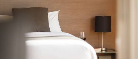 A neatly made bed with white and brown bedding, a bedside table with a glass of red wine, and a modern lamp.