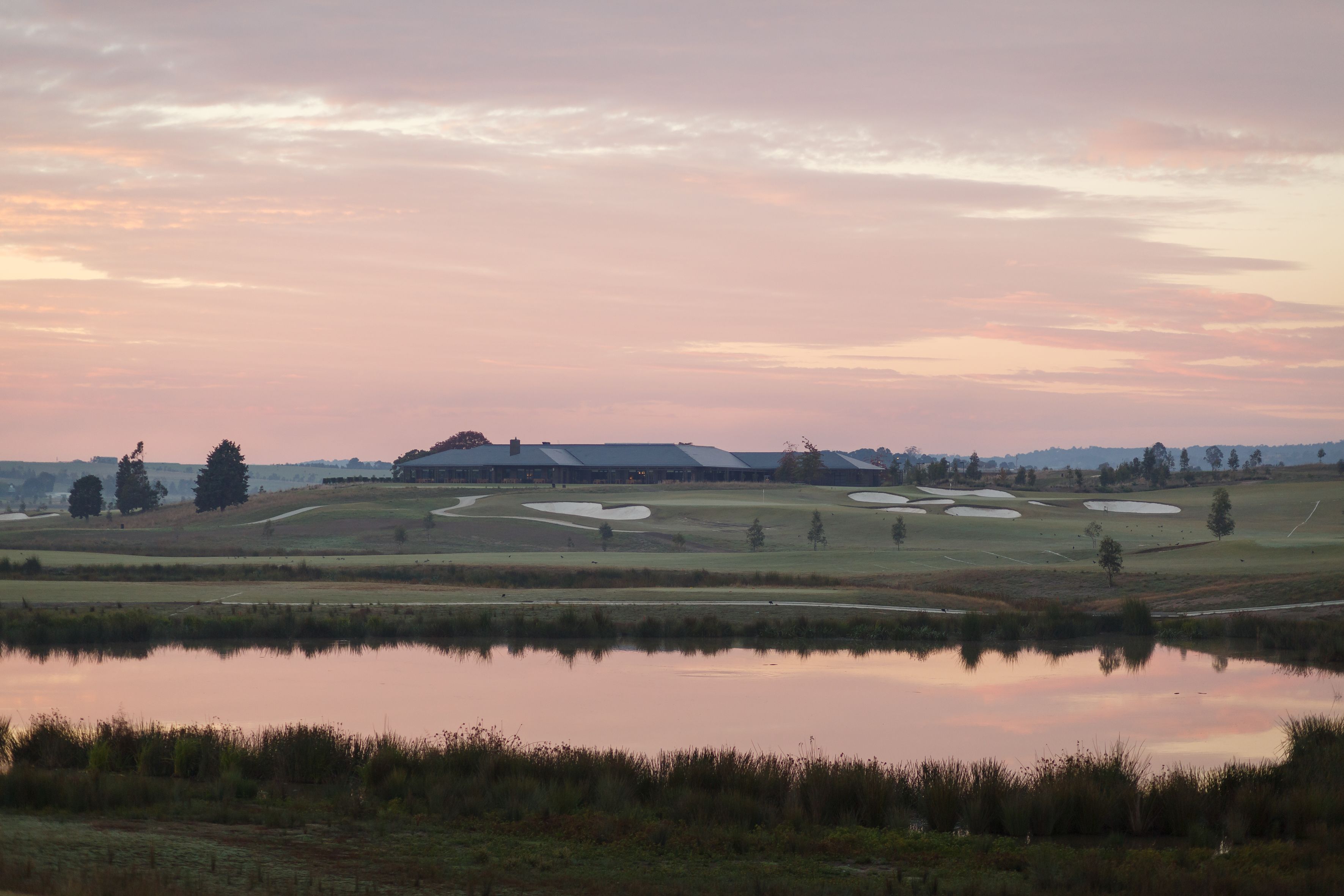 Un campo de golf con búnkeres, un estanque y un edificio al fondo.