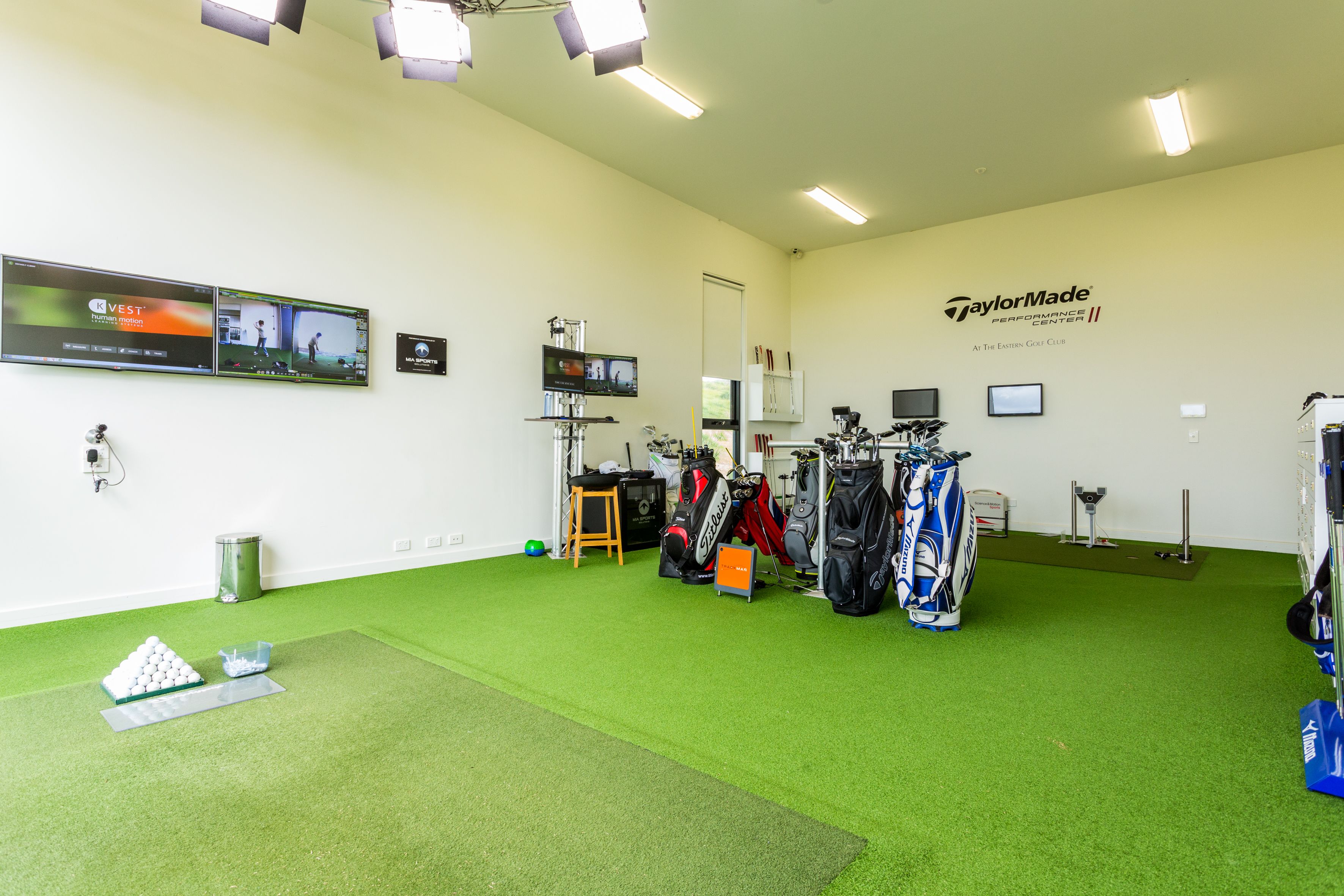 A golf practice area with artificial turf, golf bags, and a TaylorMade Performance Center sign.