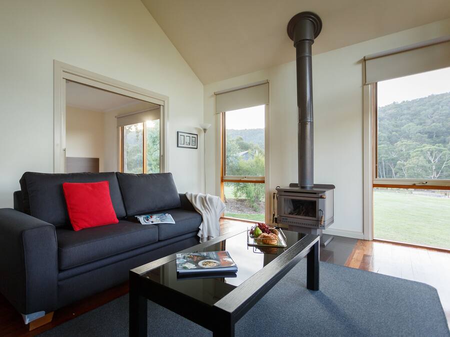 A modern living room with a black sofa, a glass coffee table, and a wood-burning stove.