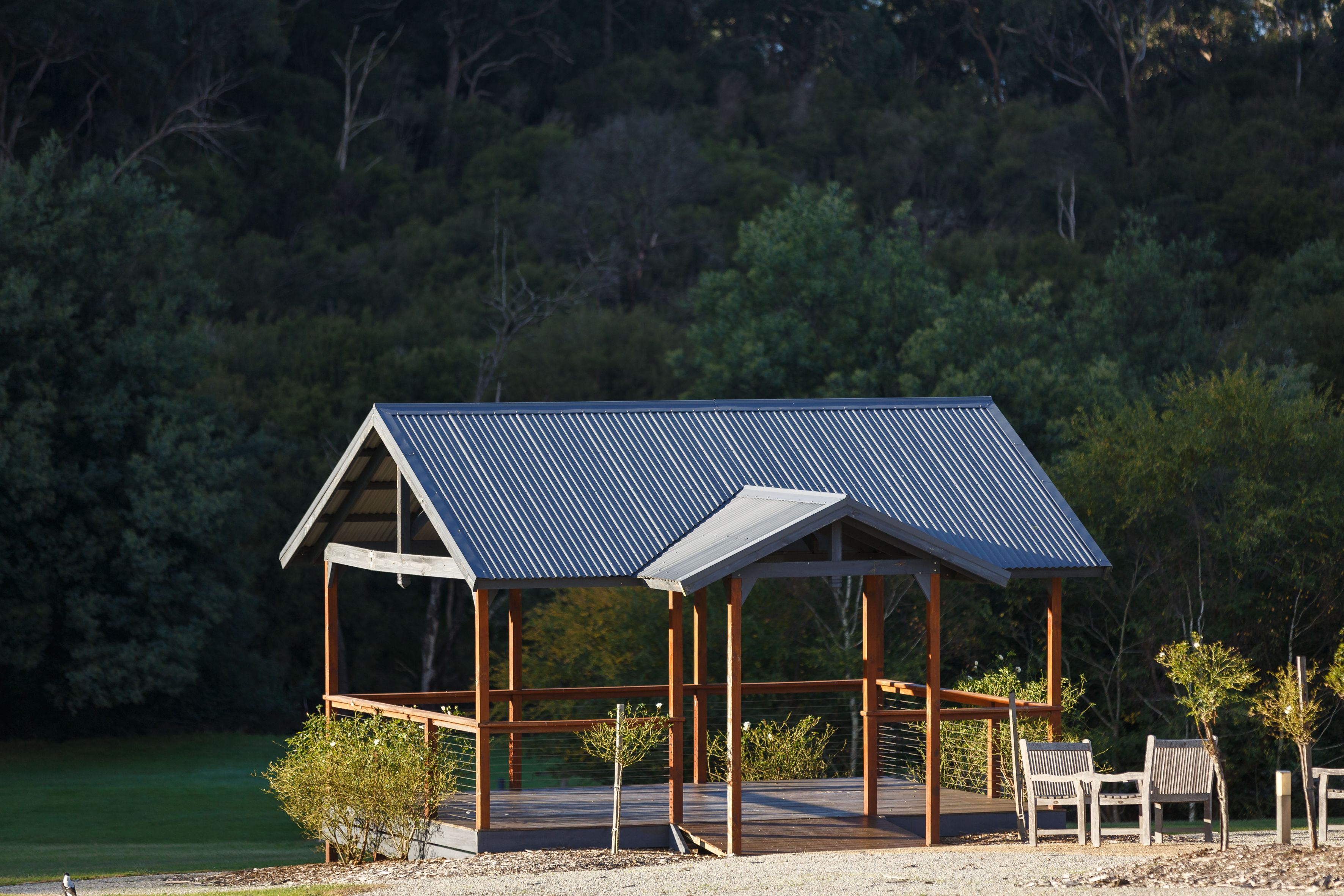 Un gazebo in legno con tetto in metallo affaccia su un lago, circondato da alberi.
