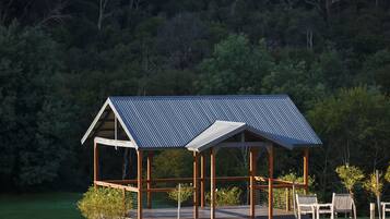 Un gazebo in legno con tetto in metallo affaccia su un lago, circondato da alberi.
