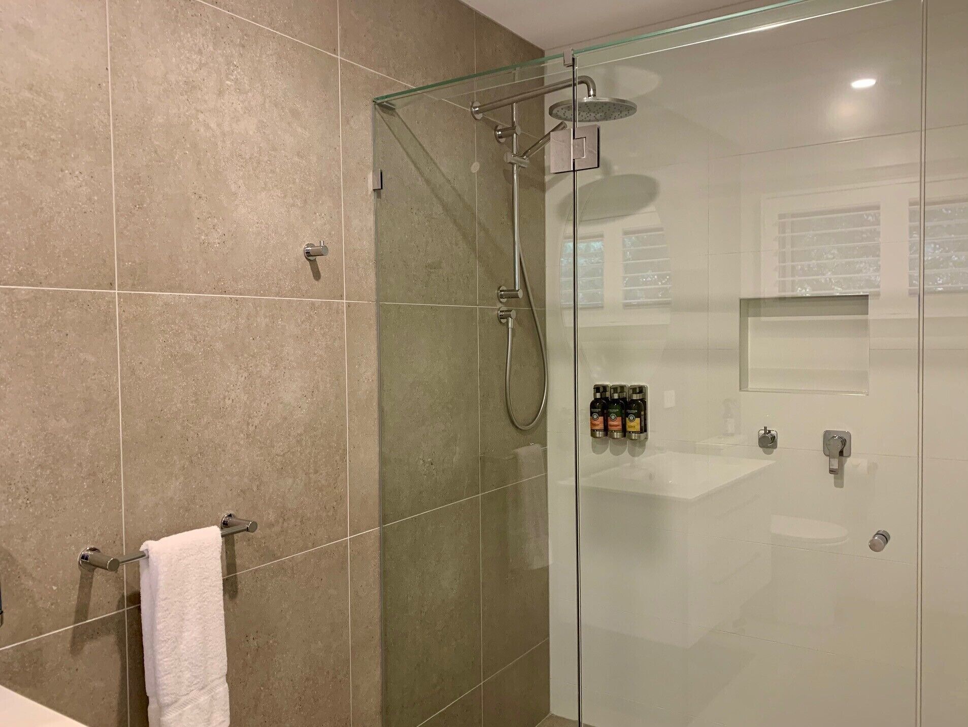 A modern bathroom with a glass-enclosed shower, a white sink, and a towel rack.
