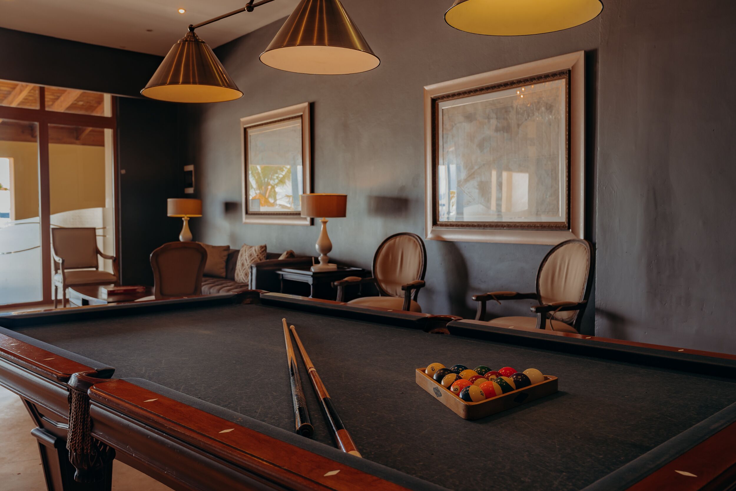 A pool table with a cue stick, a tray of billiard balls, and two lamps.