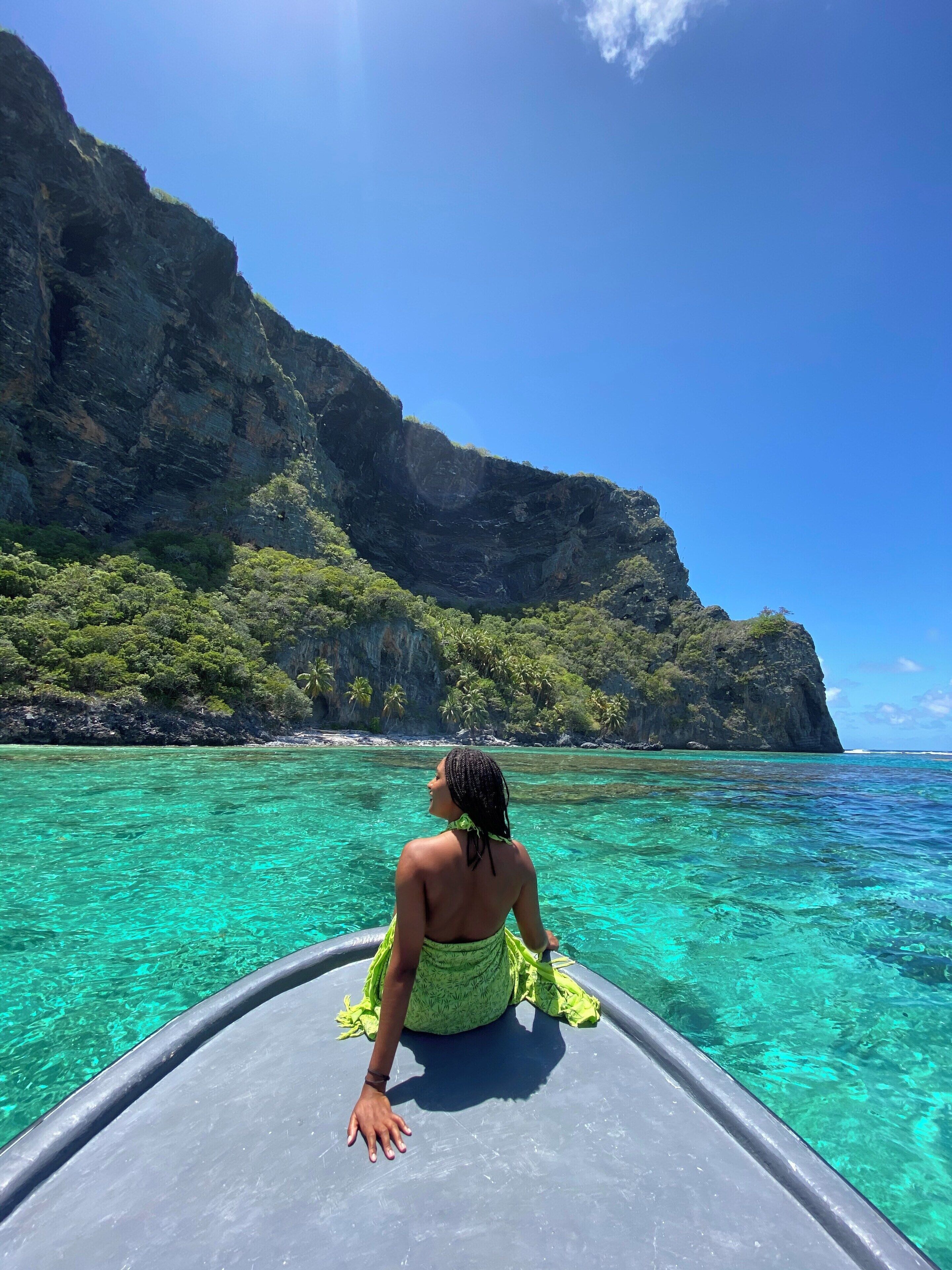 Una persona sentada en un bote disfrutando de una costa montañosa y aguas turquesas.