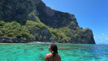 Una persona sentada en un bote disfrutando de una costa montañosa y aguas turquesas.
