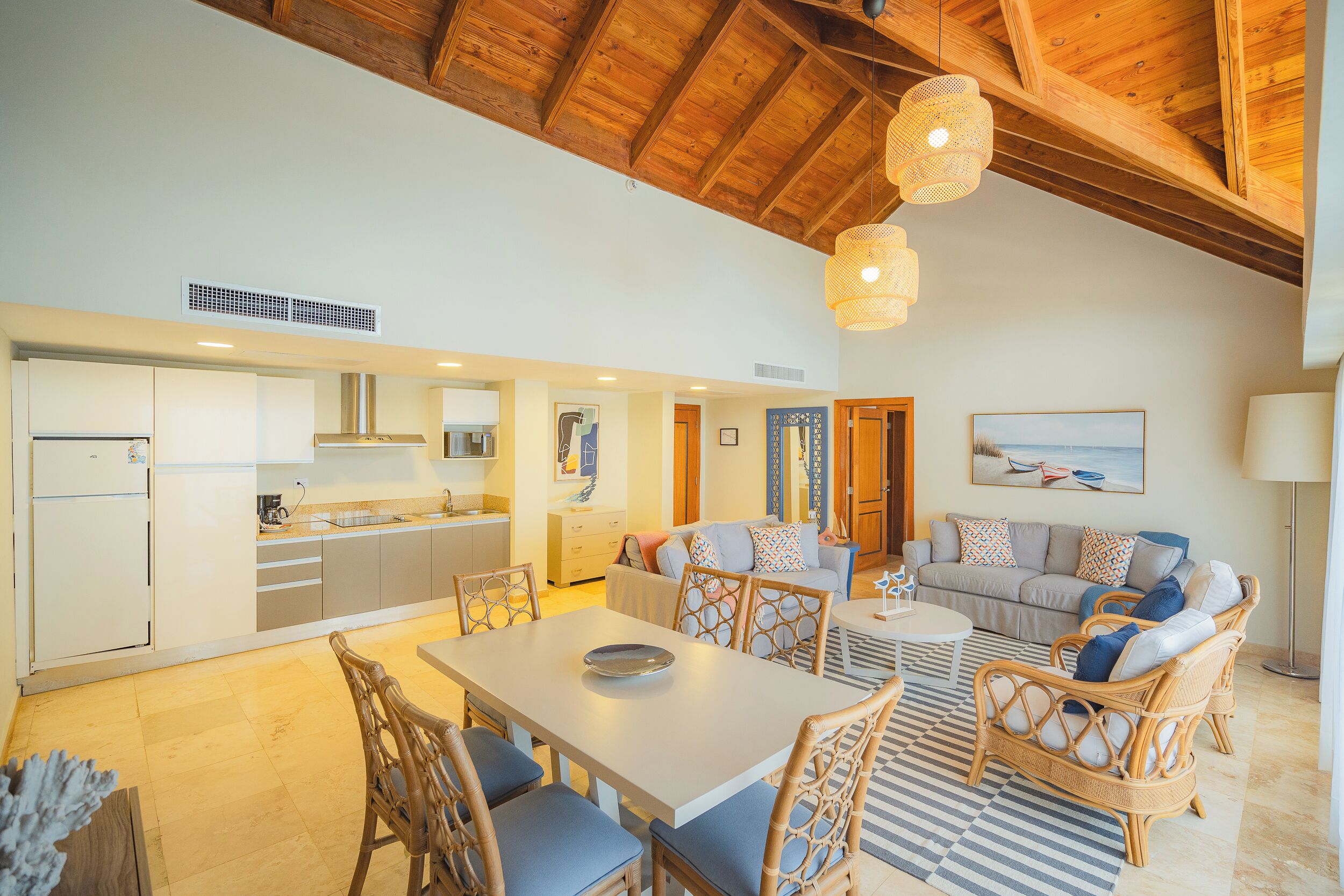 A spacious living area with a dining table, wicker chairs, a sofa, and a kitchen in the background.