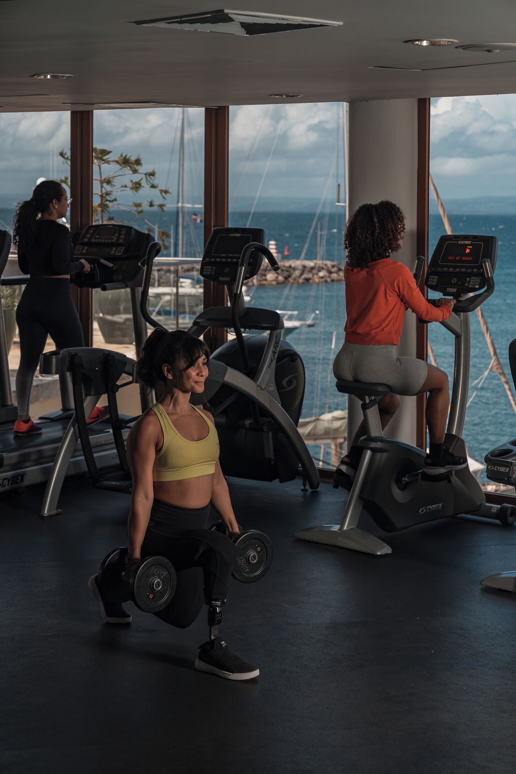 A gym with treadmills and weights, large windows with a view of the sea.