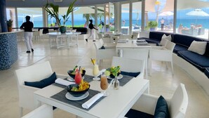 A spacious indoor area with white furniture, a dining table with drinks, and a view of the ocean. -  Bannister Hotel &  Yacht Club (Samaná)