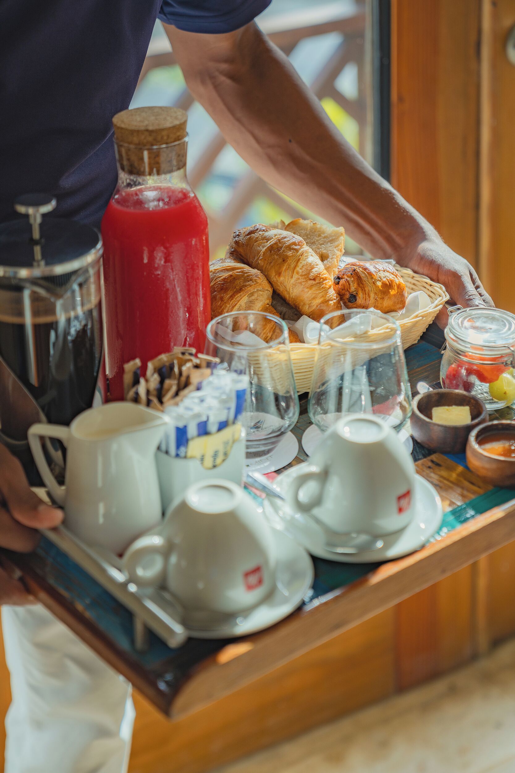 Bandeja de desayuno con cruasanes, una bebida roja y diversos productos para el desayuno.