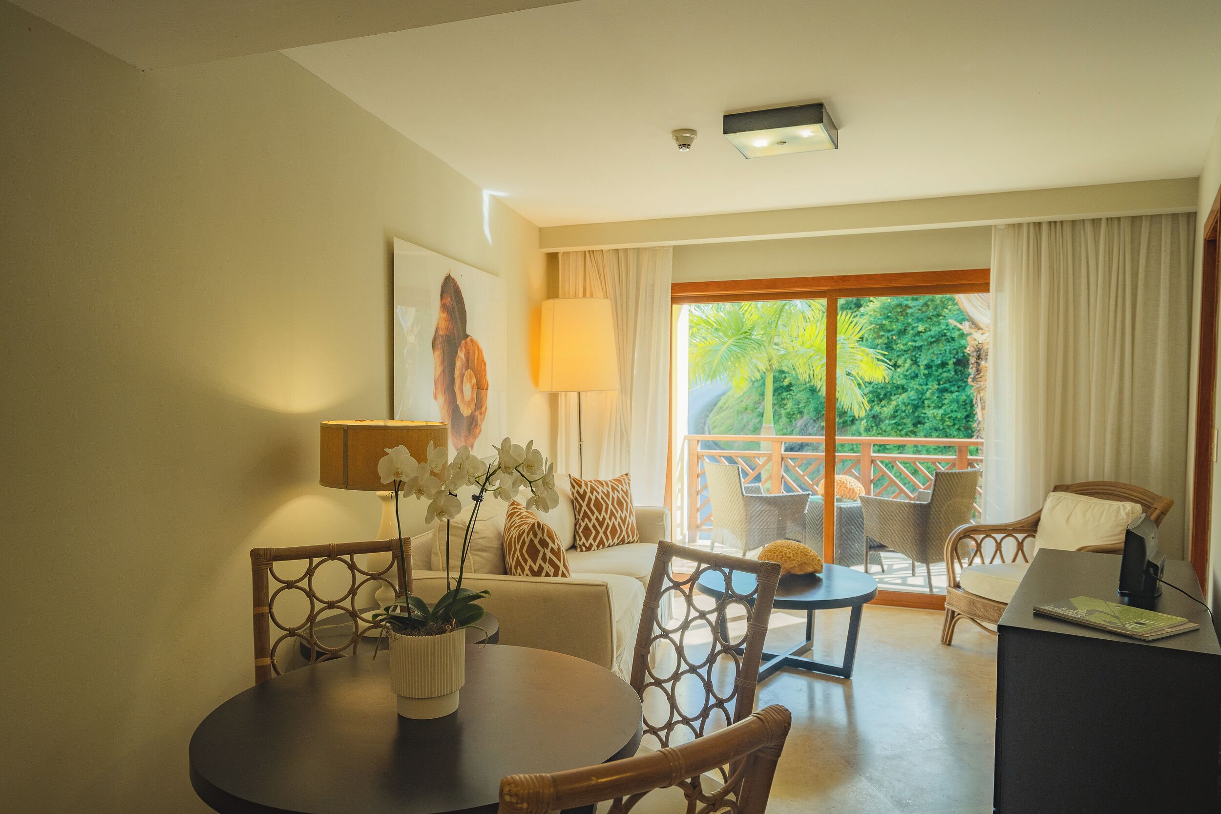 A hotel room with a balcony, a dining area with a table and chairs, and a seating area with a sofa and armchairs.