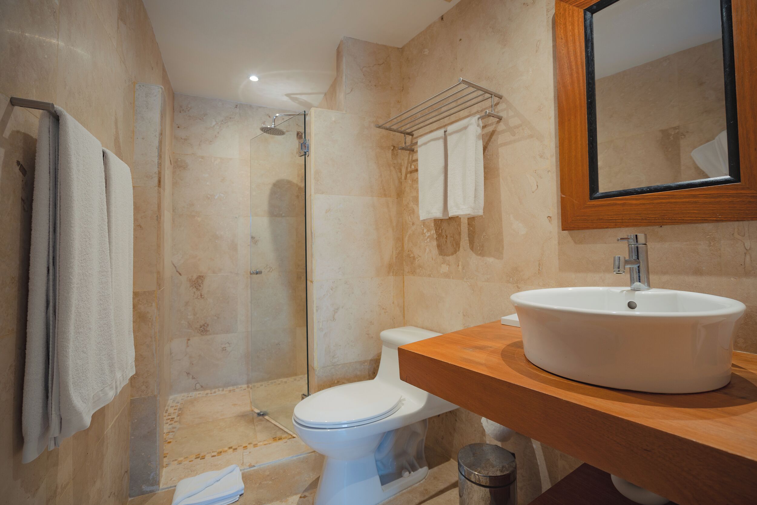 Een moderne badkamer met een glazen douchecabine, een wit toilet en een houten wastafelmeubel met een wastafel.