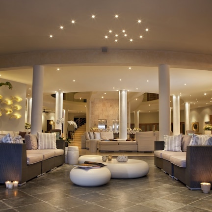 A spacious lobby with a curved seating area, a staircase, and a large plant.