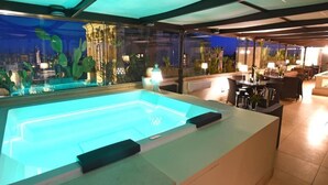 Piscina interior climatizada con asientos y vistas a un paisaje urbano nocturno.