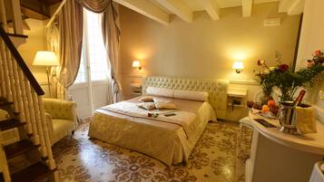 Un dormitorio con una cama grande, una zona de estar con una silla, una mesita pequeña y un jarrón decorativo con flores.