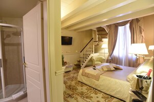 Habitación de hotel con cama, silla, televisión, escalera y ducha.