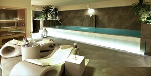 A spa area with three reclining chairs, a glass-enclosed pool, and a waterfall feature. - SANTA CHIARA Suite Hotel & Spa - Lecce (Lecce)