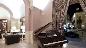 A grand piano in a well-lit lobby with marble flooring, a leather sofa, and a table with a lamp. - SANTA CHIARA Suite Hotel & Spa - Lecce (Lecce)