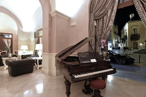 Een vleugelpiano in een goed verlichte lobby met marmeren vloeren, een leren bank en een tafel met een lamp.