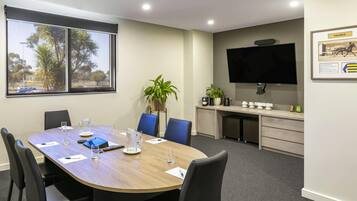 A conference room with a large table, chairs, a TV, and a window with a view of palm trees.