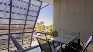 A balcony with a table and chairs, a view of a parking lot, and a building with a modern design. - Mantra Melbourne Melton (Cobblebank)