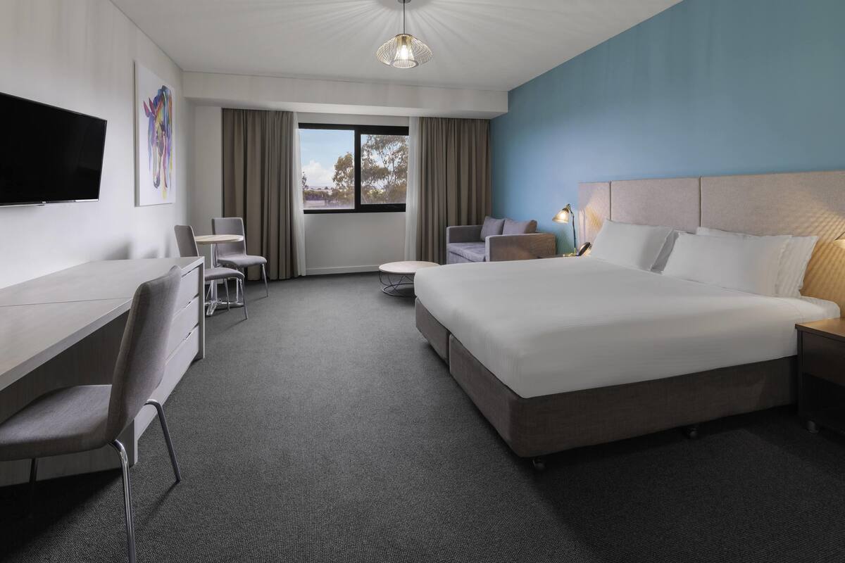 A hotel room with a bed, desk, chair, TV, and a view of the outdoors.