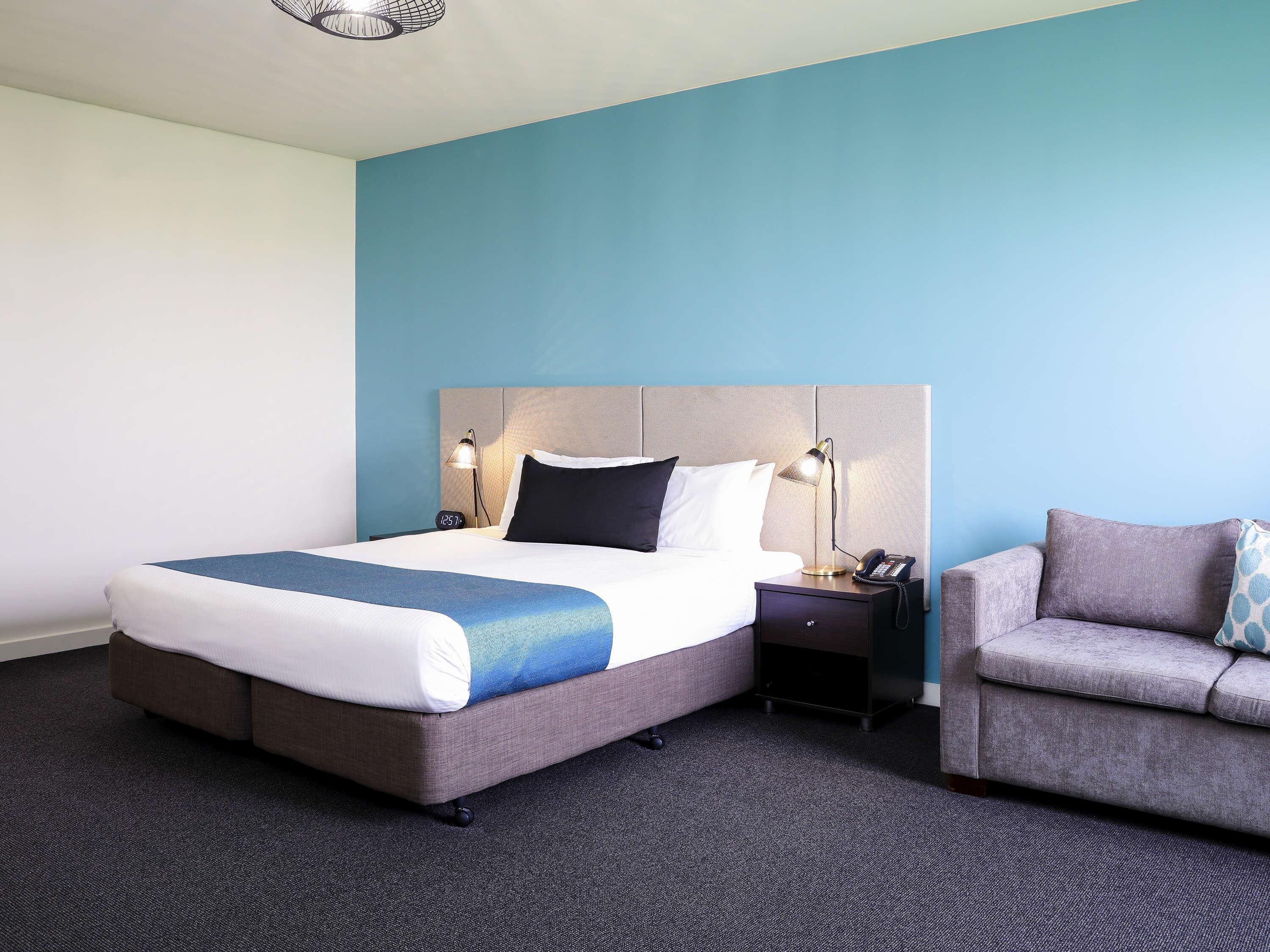 A hotel room with a bed, bedside tables, a lamp, a clock, and a sofa.