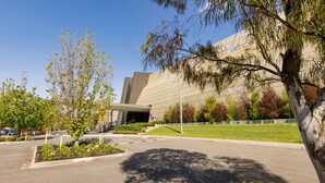 A modern building with a parking lot, a landscaped area with trees, and a clear sky. - Mantra Melbourne Melton (Cobblebank)