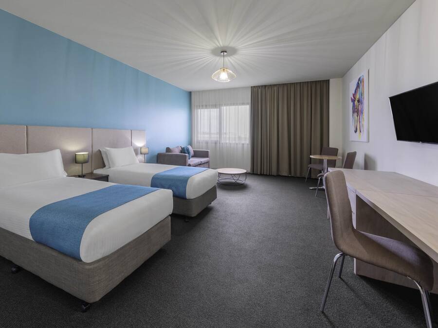 Una habitación de hotel con dos camas, un escritorio, una silla, una mesita y un televisor.