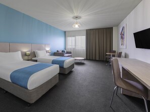 A hotel room with two beds, a desk, a chair, a small table, and a TV. - Mantra Melbourne Melton (Cobblebank)
