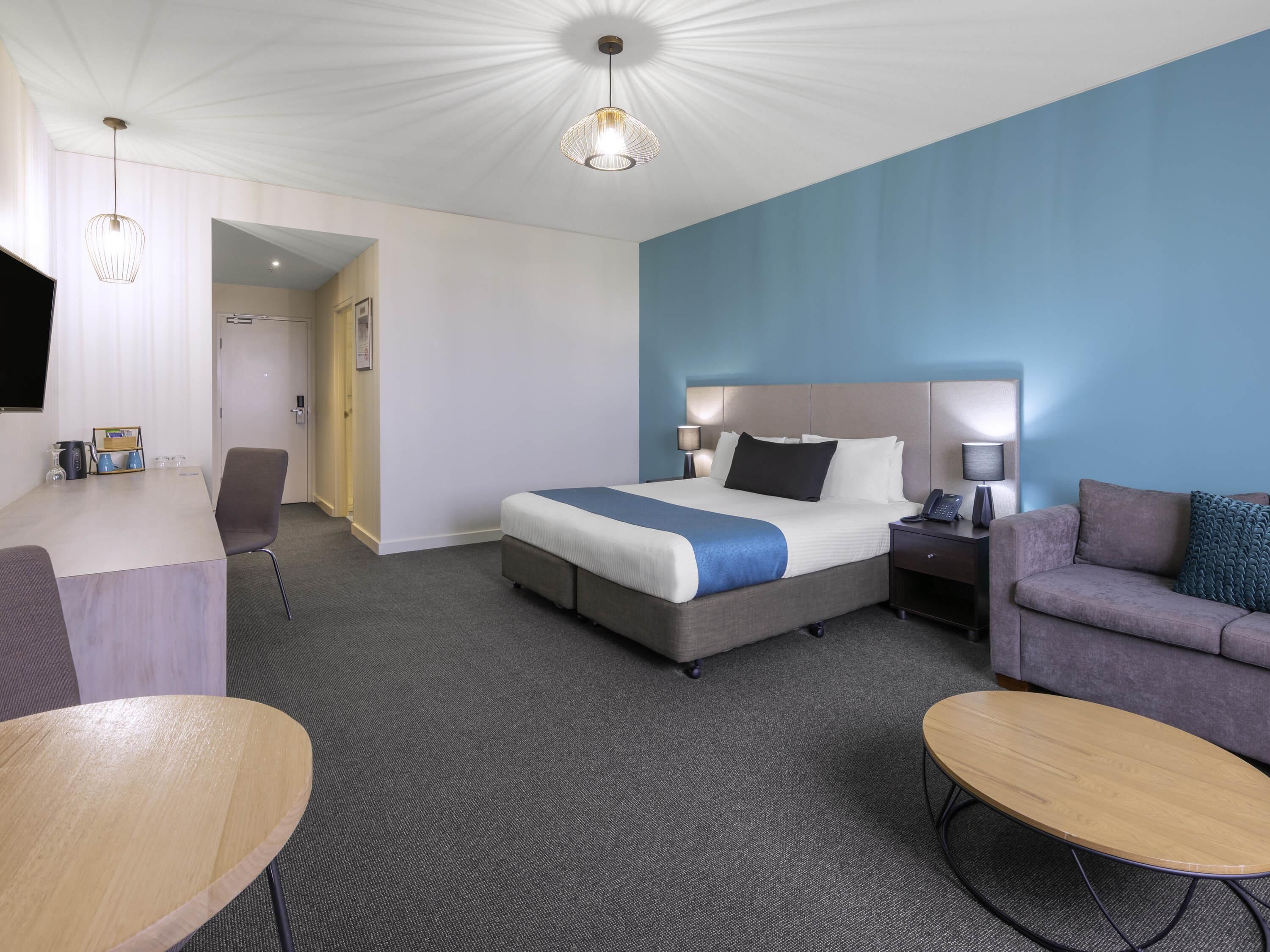 Una habitación de hotel con cama, escritorio, sofá, mesa redonda y lámpara.