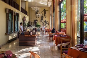 A spacious restaurant with high ceilings, a chandelier, and large windows offering a view of the outdoors.