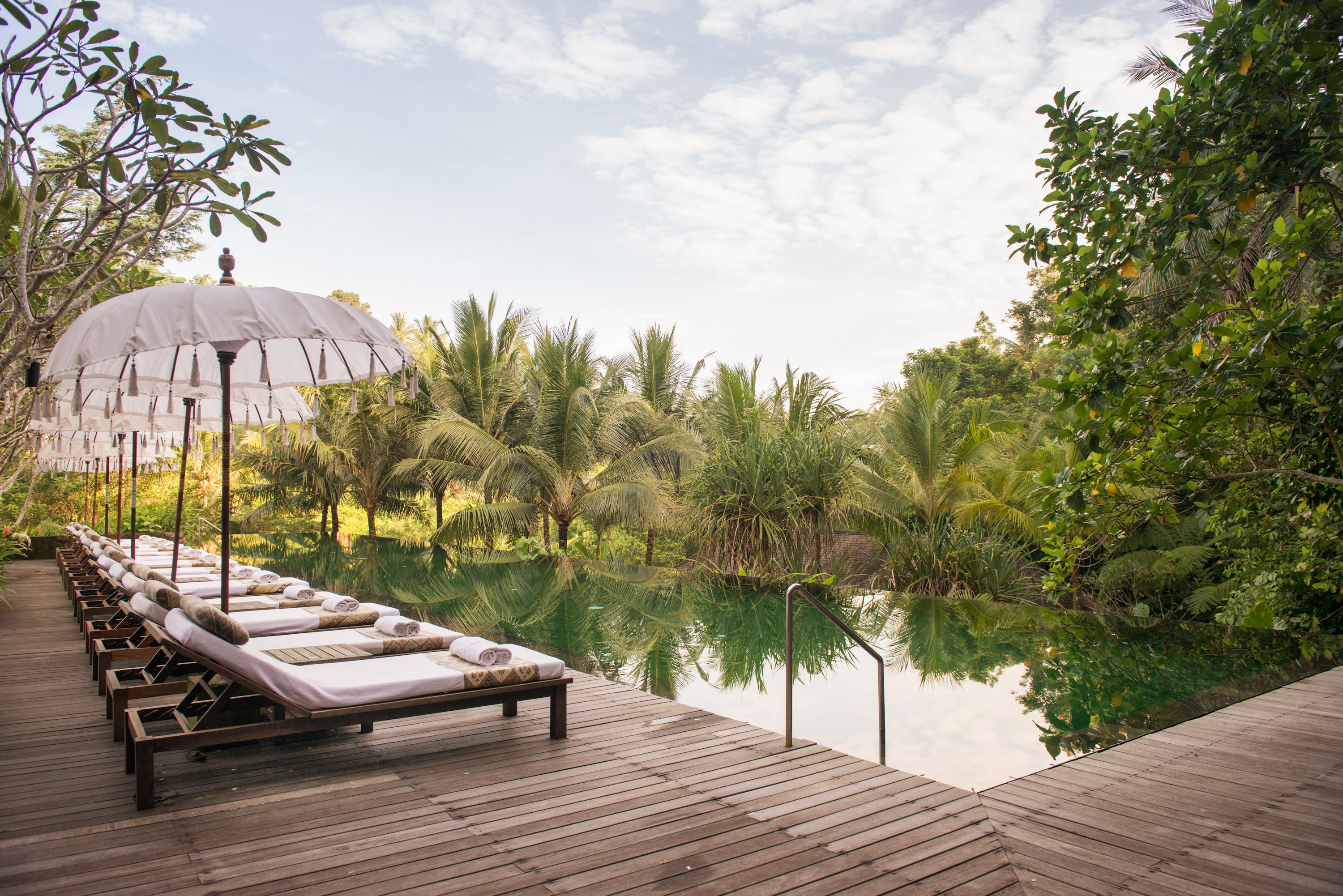 A wooden deck with lounge chairs and a canopy, overlooking a calm body of water and lush greenery.