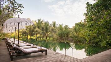 A wooden deck with lounge chairs and a canopy, overlooking a calm body of water and lush greenery.