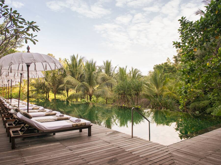 A wooden deck with lounge chairs and a canopy, overlooking a calm body of water and lush greenery.