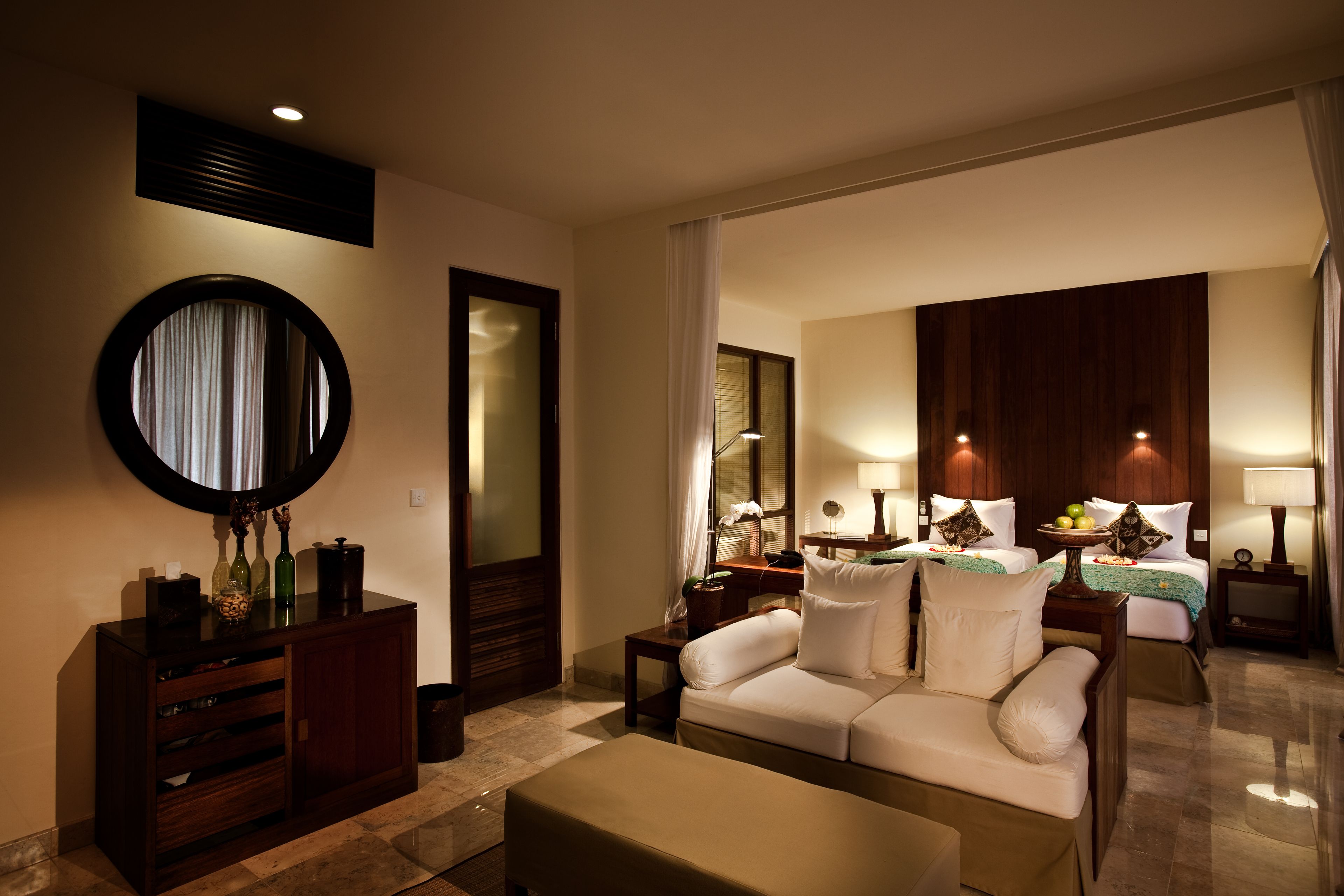 A hotel room with a sofa, a small table, a mirror, a cabinet, and a bed with a nightstand.
