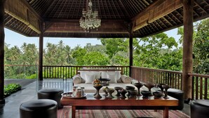 Un espacio de estar techado al aire libre con vistas a palmeras, una piscina y una mesa con diversos objetos.