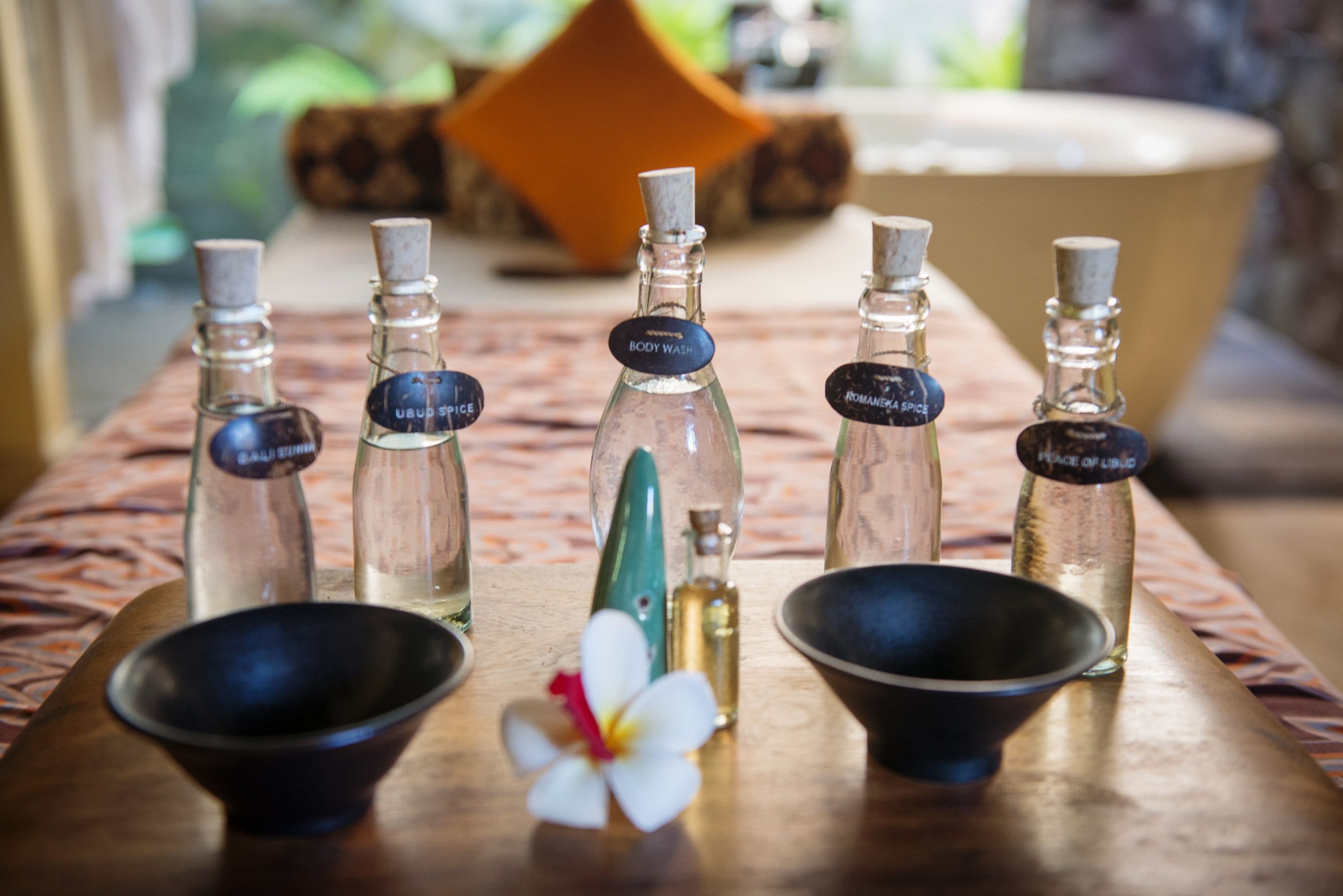 A wooden table with five glass bottles labeled with different scents and two black bowls.